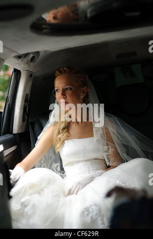 Braut im Hochzeitskleid sitzt in Limousine und im Fenster schaut. Stockfoto