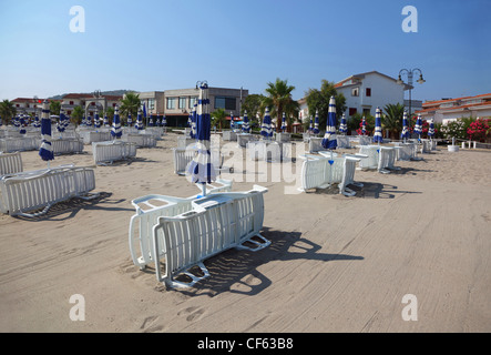 viele weiße gestreifte Liegestühle und Sonnenschirme sind am leeren Strand. Stockfoto