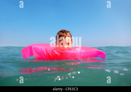 Der kleine Junge schwimmend im Meer auf aufblasbare rosa Matrese. erschossen von Unterwasser-Box, Wasser auf dem Feld verschwommen