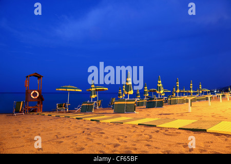 Abend gebaut, Liegestühle und Sonnenschirme und Kautschuk-Pfad, der zur Rettung Stand dient stehen am Strand Stockfoto