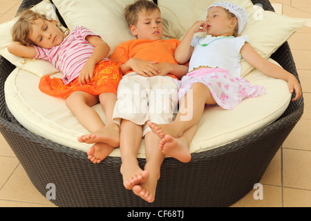 zwei müde Mädchen und jungen am großen Kreis-Sessel mit Kissen liegen und erholend Stockfoto