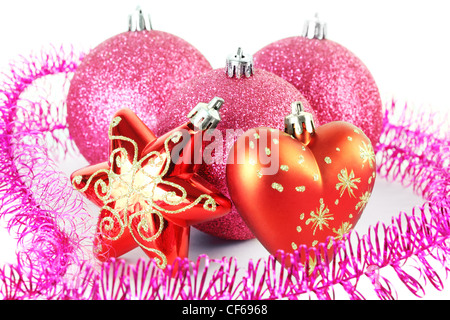 Drei rote Christbaumkugeln hinter Sterne und Herzen umgeben von lila Lametta Stockfoto
