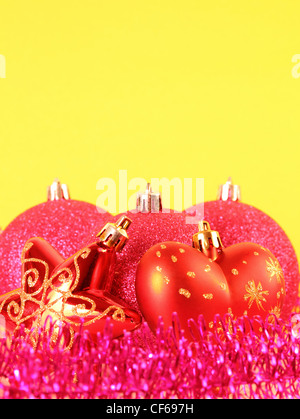 Top drei rote Christbaumkugeln hinter Stern Herz umgeben von lila Lametta isoliert auf gelben Stern Herz im Fokus. Stockfoto