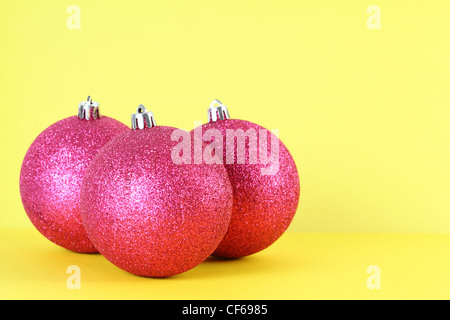 Drei rote Christbaumkugeln isoliert auf gelb, Fokus auf vorderen ball Stockfoto