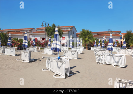 viele Lounges und Sonnenschirme am Strand in der Nähe von Palmen und Häuser, sonnigen Tag Stockfoto