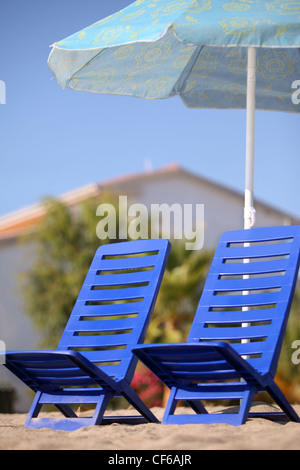 Zwei dunkle blaue leere Stühle stehen unter Sonnenschirm, Fokus auf linken Stuhl Stockfoto