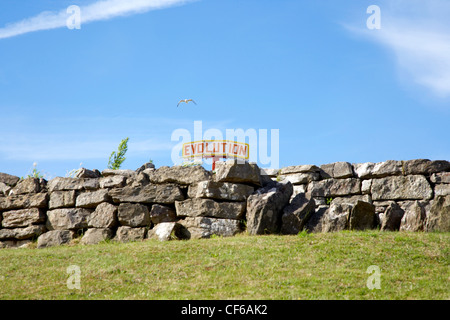 Die Oberseite einer Kirmes-Fahrt ist sichtbar hinter einer alten Steinmauer auf Barry Island in Glamorgan. Stockfoto