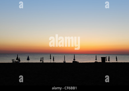 Silhouetten von geschlossenen Sonnenschirme und Liegestühle am Strand bei Sonnenuntergang Stockfoto