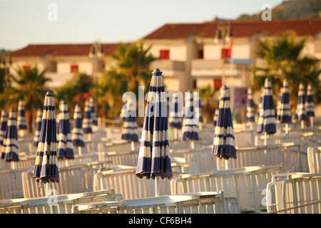 Liegestühle und Strand Sonnenschirme ordentlich gebaut Reihen am Strand morgens neben Hütten, flacher Schärfentiefe Stockfoto