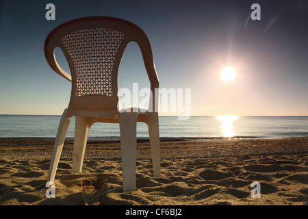 Einem weißen Plastikstuhl steht seitlich am Strand in der Nähe von Meer in der Morgendämmerung Stockfoto