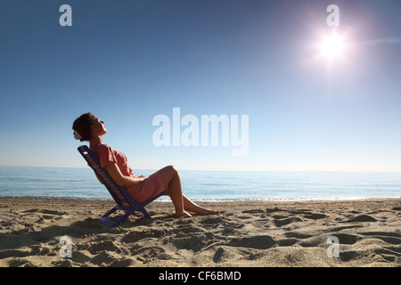 Frau sitzt auf Plastikstuhl am Meeresufer von Person, die Sonne und wird gegerbt, wogenden Kopf Stockfoto