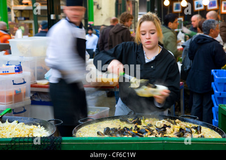 Ein junges Mädchen servieren Paella im Borough Market in London. Stockfoto