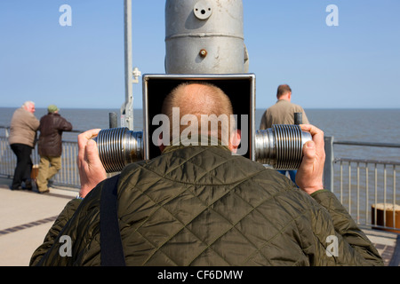 Ein Mann peering hinaus auf das Meer mit einem Teleskop hat eine Roboter aussehen gewonnen. Stockfoto