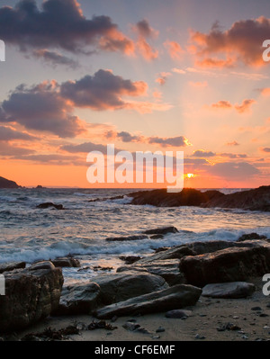 Ebbe am See Rock Beach, Talland Bay, wie die Sonne steigt und die Wolken beleuchtet. Stockfoto