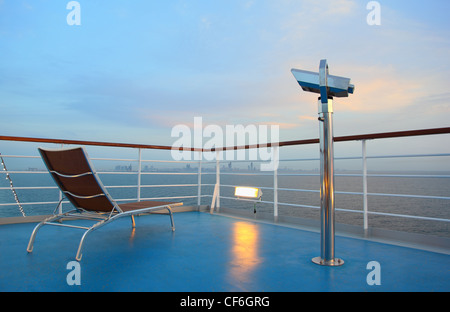 Beleuchtete einsame Liegestuhl und Fernglas auf Schiff mit Blick auf die Stadt am Abend Stockfoto