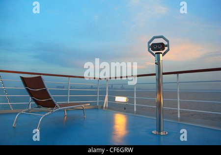 Beleuchtete einsame Liegestuhl und Fernglas für mit Blick auf Stadt Abend auf Schiff Stockfoto