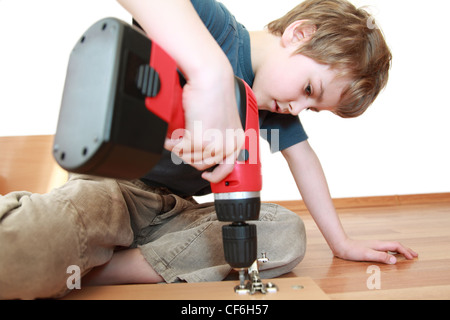 Kleiner Junge auf dem Boden liegend und festziehen der Schrauben in Holzbrett Stockfoto