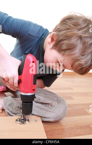 Kleiner Junge auf dem Boden sitzend und festziehen der Schrauben in Holzbrett Stockfoto