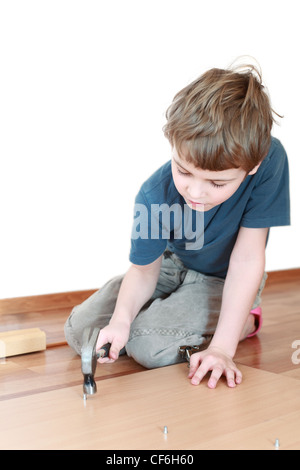 Kleiner Junge sitzt auf dem Boden und fleißig hämmert Nagel in Holzbrett Stockfoto