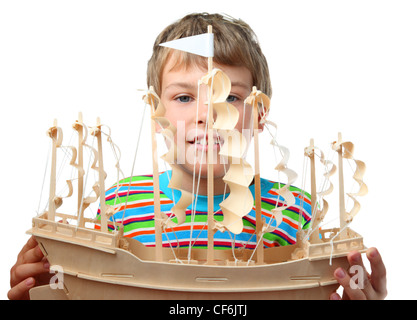 Kleiner Junge im gestreiften Shirt hält künstliche Holzschiff mit Papier-Segeln Stockfoto