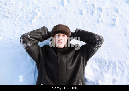 Junger Mann liegt am Rücken auf Schnee suchen Hände zum Kopf und schaut verträumt Stockfoto