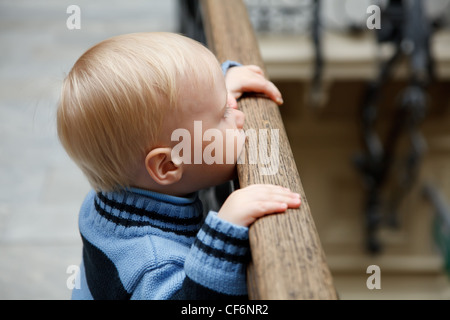 Kleiner Junge steht am Zaun festhalten an Geländer und schaut nach unten. Stockfoto