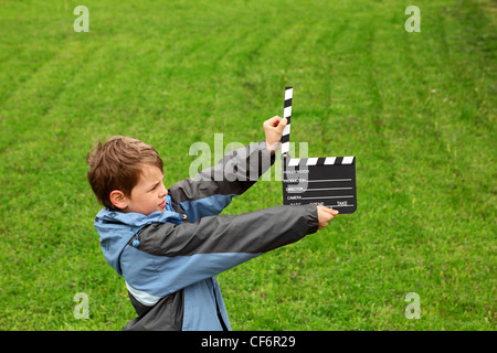 Jungen Jacke mit Kino Klappe in ihren Händen auf Feld mit grünen Rasen stehen Stockfoto