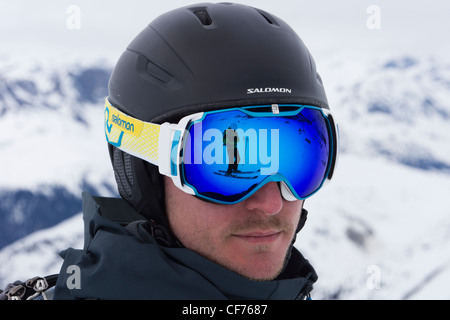 Mann mit Salomon Ski Helm mit einem Skifahrer auf Schnee reflektiert in einem Paar von blau Skibrillen Stockfoto