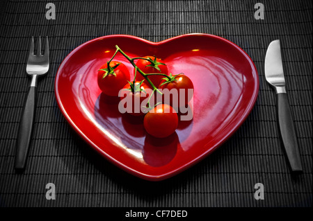 Strauchtomaten auf Rotes Herz-förmige Platte, mit Tisch Gesunde frische Essen Regime. Stockfoto