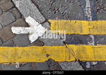 Detail von Straßenmarkierungen auf einem Fußgängerüberweg gemalt: ein weißer Pfeil nach rechts und gelben Linien. Stockfoto