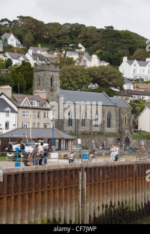 Familien-Krabben fischen an der Pier in Aberdovey vor bunte Strandhäuser vorne und St.-Peter Kirche, Aberdyfi, Wales, UK Stockfoto