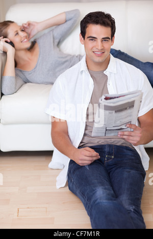 Man lehnt sich an das Sofa mit Zeitung, während seine Freundin Musik hört Stockfoto