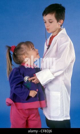 Ein kleiner Junge gibt sich ein Arzt und hört den Herzschlag eines kleinen Mädchen-Patienten mit einem Stethoskop. Stockfoto