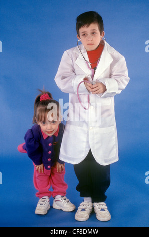 Ein kleiner Junge gibt sich ein Arzt und hört den Herzschlag eines kleinen Mädchen-Patienten mit einem Stethoskop. Stockfoto