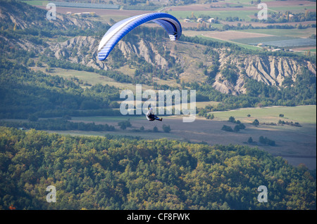 Ein Gleitschirmflieger schweben hoch über dem Talboden mit landwirtschaftlich genutzten Flächen unter in Le Chabre, Provence. Stockfoto