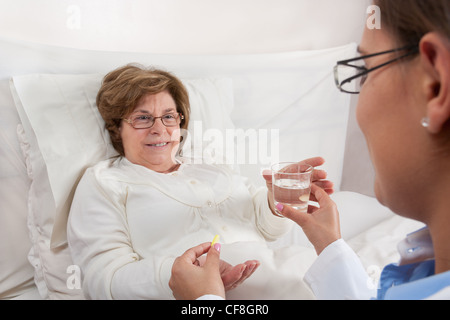 Arzt, sitzen im Bett, gibt Medikamente und ein Glas Wasser zum Wiederherstellen von älteren Patienten Stockfoto