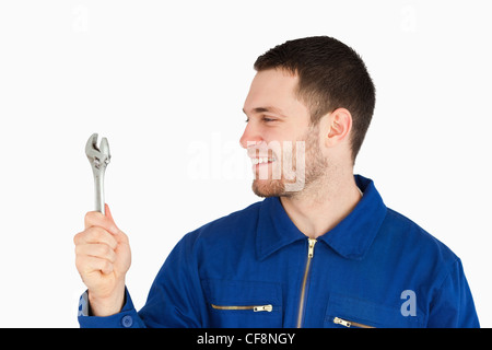 Lächelnde junge Mechaniker im Blaumann Blick auf seine Schraubenschlüssel Stockfoto