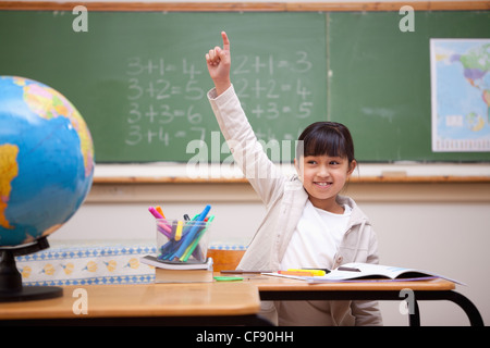 Lächelnd Schulmädchen hob ihre Hand auf eine Frage Antworten Stockfoto