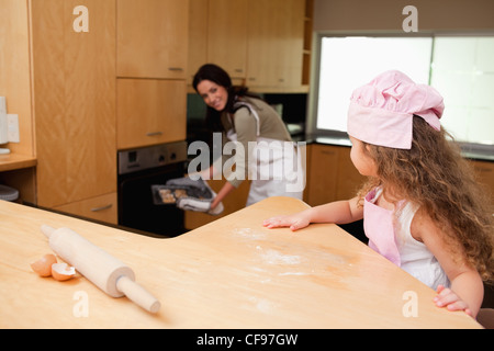 Mädchen, die gerade ihre Mutter setzen Cookies in den Ofen Stockfoto