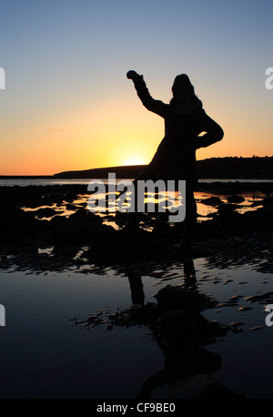 Ein Schuss von einem Silhouettiert Abbildung mit ihren Arm in die Luft vor einer irischen Sonnenuntergang über dem Atlantischen Ozean. Stockfoto