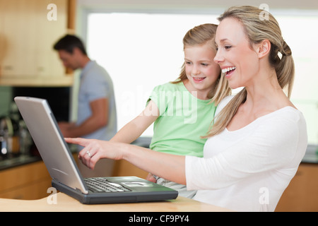 Glückliche Mutter und Tochter mit Laptop mit Vater im Hintergrund Stockfoto