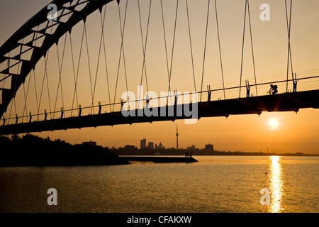 Radfahrer kreuzen Humber River Fußgängerbrücke bei Sonnenaufgang mit Toronto Skyline im Hintergrund, Toronto, Ontario, Kanada. Stockfoto