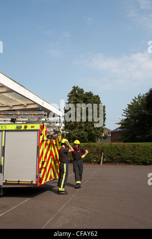 Zwei Feuerwehrmänner, die im August in Westbourne Fire Station, Westbourne, Bournemouth, Dorset, Großbritannien, mit einem Feuerwehrmann stehen Stockfoto