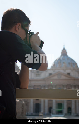 Hübscher Junge männliche Touristen fotografieren auf dem Petersplatz im Vatikan (Petersdom im Hintergrund) Stockfoto