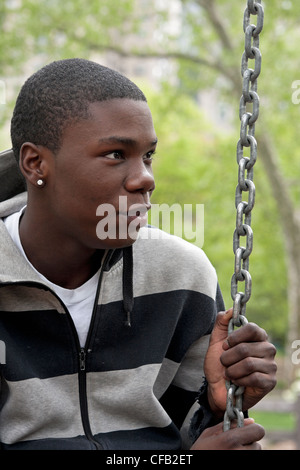 Ein Teenager im Central Park in New York City entspannt auf einer Schaukel auf einem Spielplatz. Stockfoto