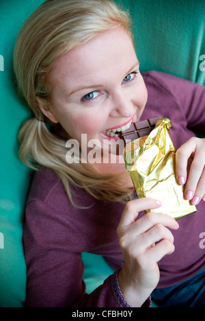 Nahaufnahme eines größeren weibliche blonde Haare aus Gesicht tragen lila Top sitzen im Sessel Haltestange Schokolade in beiden Händen Stockfoto