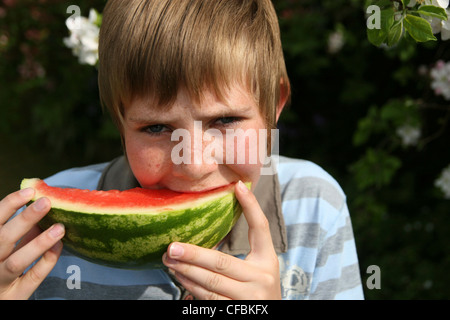 Männliches Kind mit dunkel blonde Haare trägt blaues und graues gestreiftes Top Scheibe Wassermelone essen Stockfoto