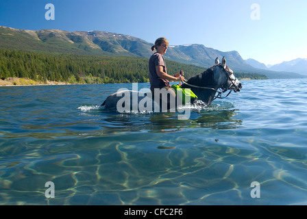 Eine junge Frau und ihr Pferd waten in den flachen, klaren Wasser der Tatla Lake, British Columbia, Kanada Stockfoto