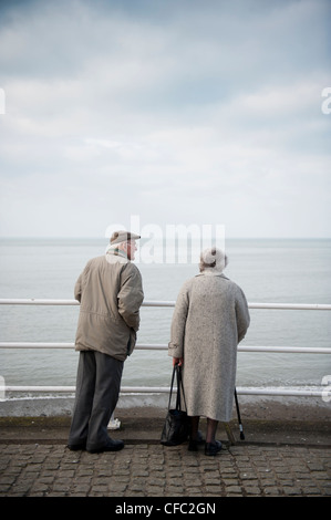 Graue Pfund: Eine Rückansicht ein älteres Ehepaar Greis und Frau gekleidet in grau, an einer Strandpromenade UK Stockfoto