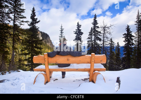 Mann sitzt mit Blick auf Tal See Holzbank Stockfoto